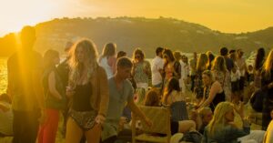 A lively gathering of people enjoying a sunset party on a beach in Mykonos, Greece.
